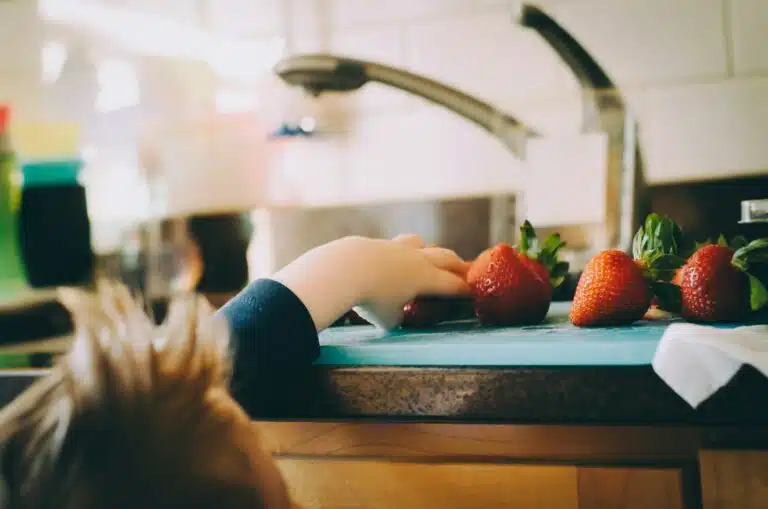 Niño recogiendo fresas en la cocina, representando la alimentación saludable en familia.